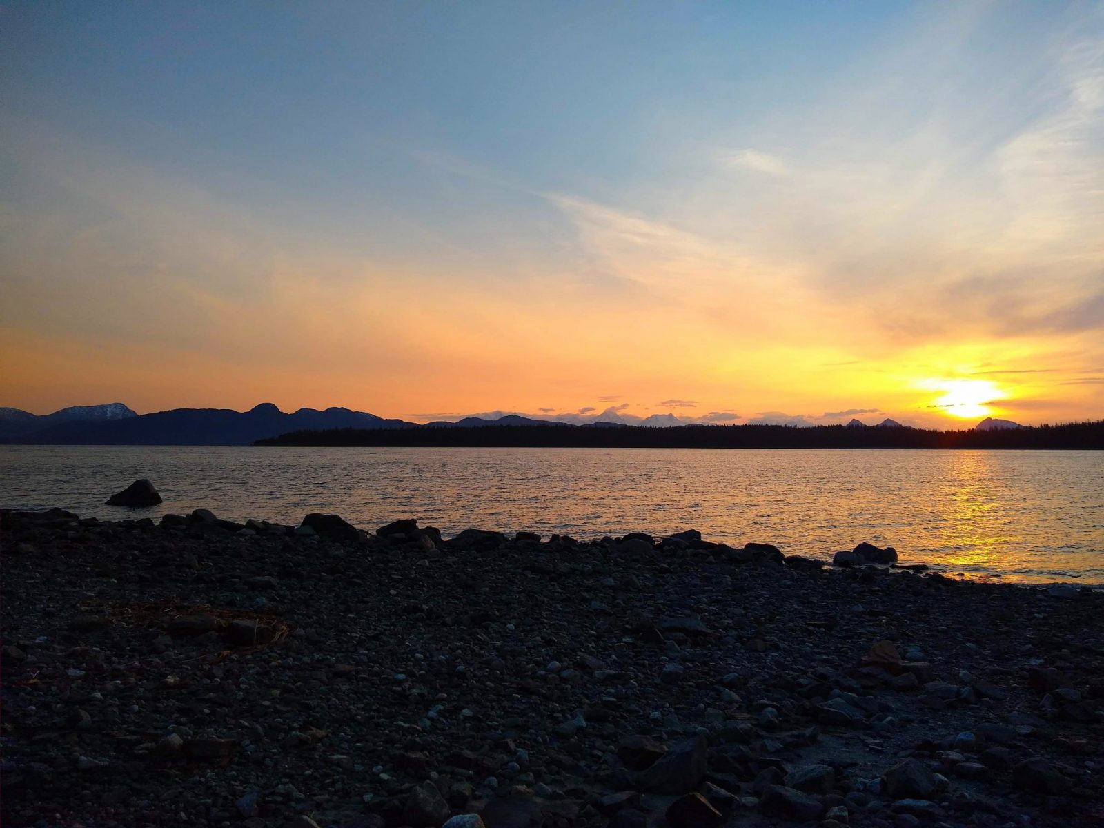 Sunset behind distant mountains across the bay from a rocky beach in the Bartlett Cove Campground in Glacier Bay National Park