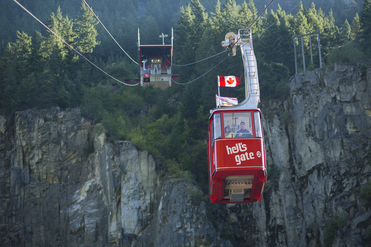 a red aerial tram car on cables going up the side of a rock and forested canyon