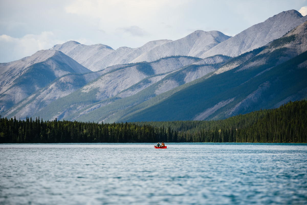 Muncho Lake along the drive to alaska with a distant canoe and two people paddling. On the other side of the lake is forest and high mountains