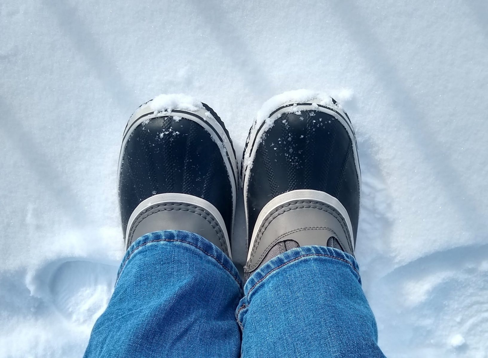 a person's lower legs wearing jeans and rubber snowboots standing in the snow