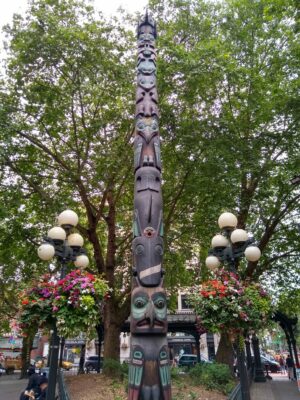 Pioneer Square, part of a Seattle Itinerary, includes trees and a high totem pole. There are also globe lanters with hanging flower baskets