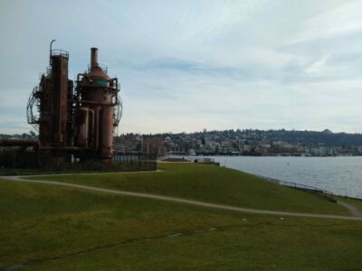 Seattle parks are an important part of a Seattle itinerary. This is gasworks park, with old rusted steam equipment sitting on a grassy hill with a trail going by. In the background is Lake Union, an urban lake in Seattle