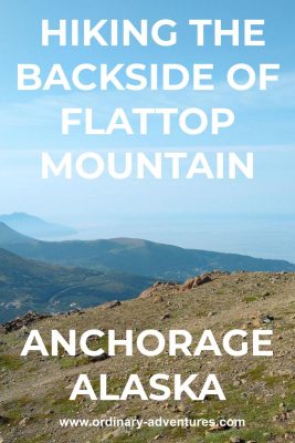 A rocky meadow with forested hillsides in the background along with the ocean in the hazy distance. Text reads: Hiking the backside of flattop mountain anchorage alaska