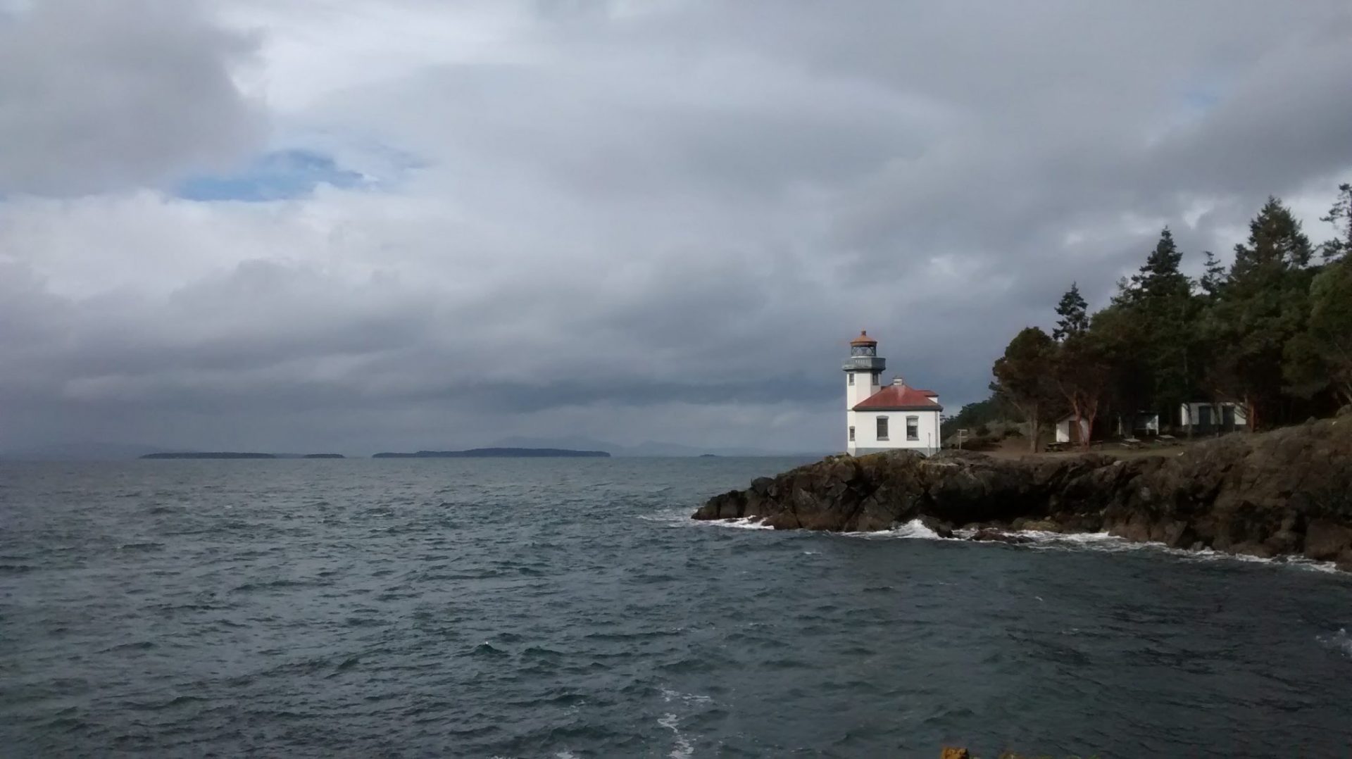 A lighthouse on the edge of a rocky bit of land next to the water, surrounded by evergreen trees at Lime Kiln State park on san juan island