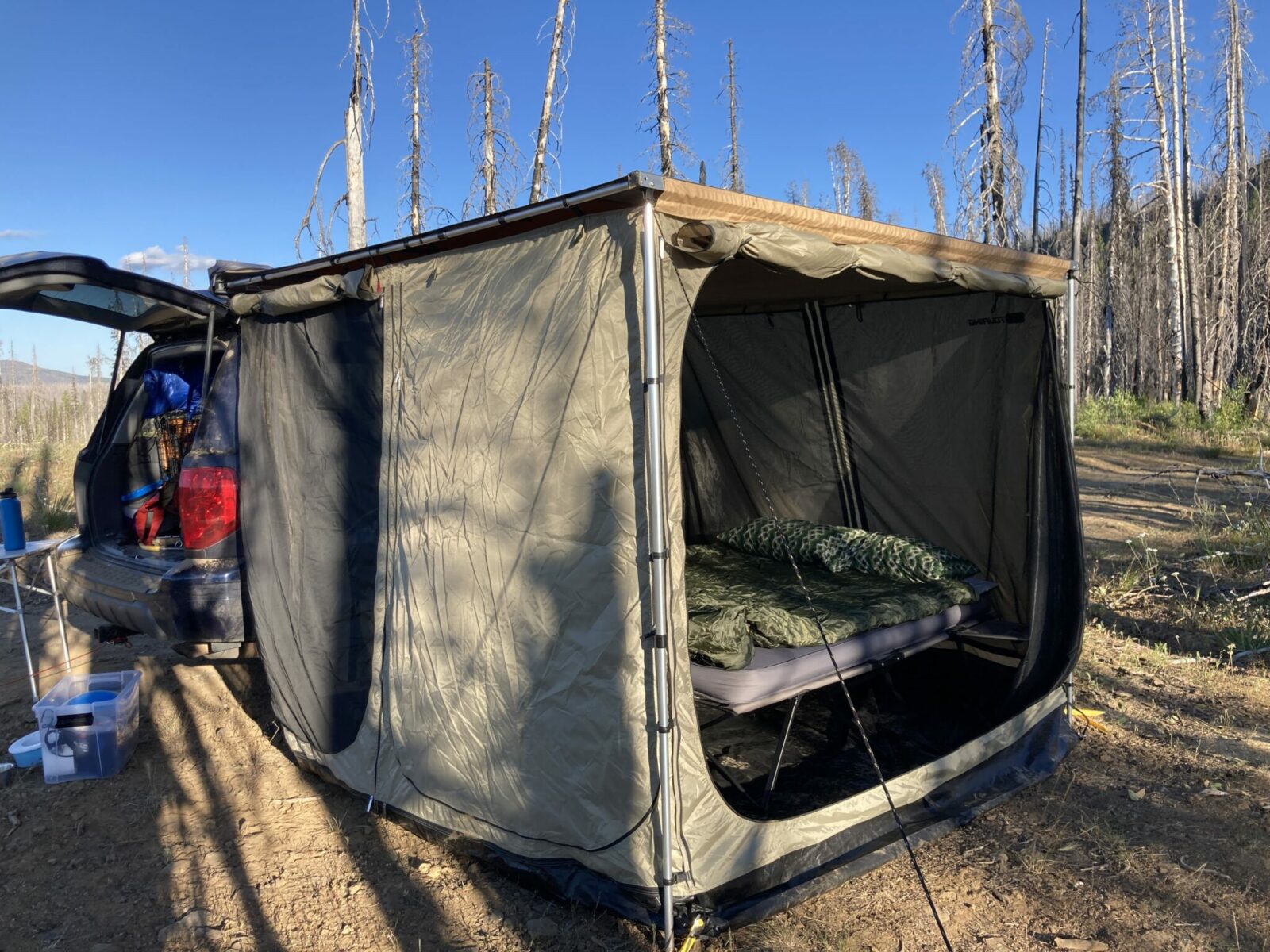 A blue suv with its hatch open and a roof top awning set up. There is a large tent attached to the sides of it. One side is open showing the bed