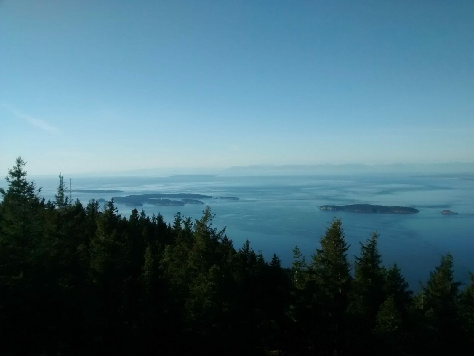 Sucia Island seen from the summit of Mt Constitution on Orcas Island. There are other islands visible in the water and a forest in the foreground and distant mountains in the hazy background