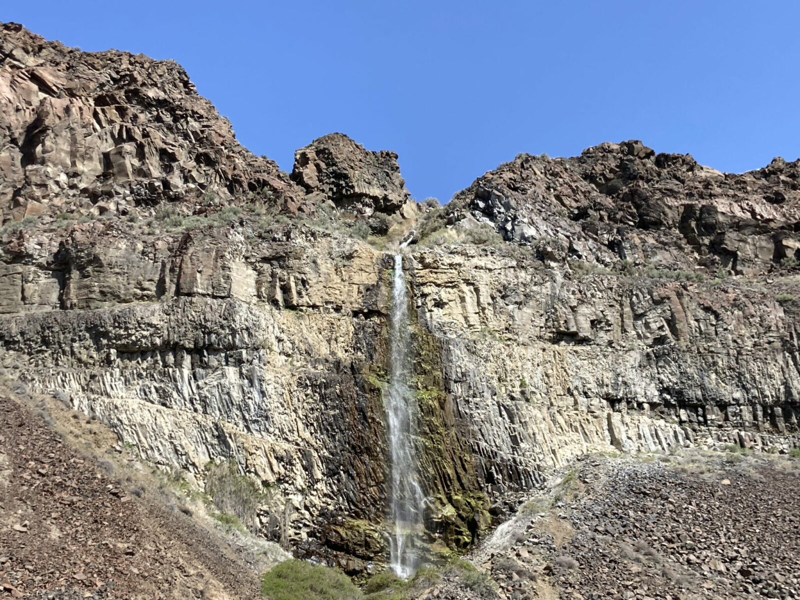 Narrow waterfall coming over vertical basalt rock on a sunny day in frenchman coulee